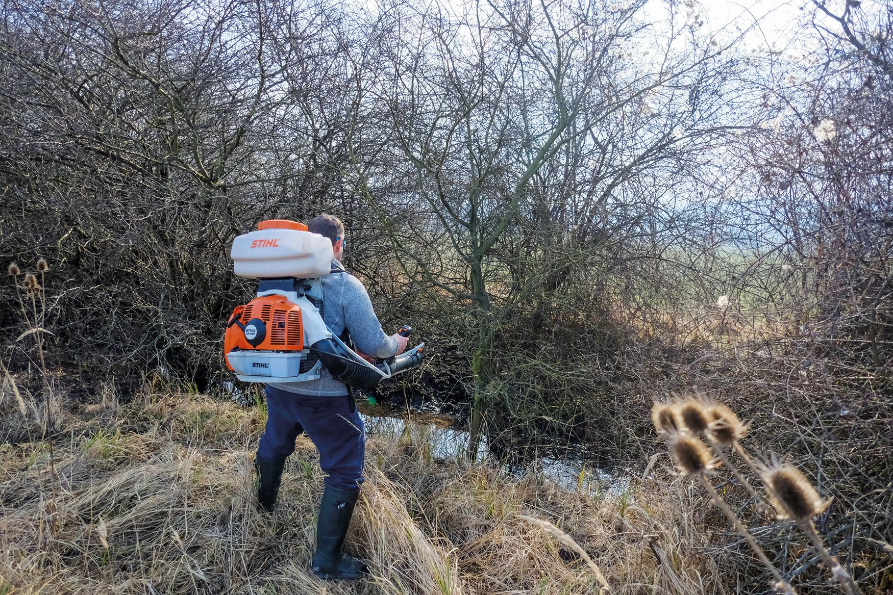 Muž s takzvaným chrličom pri vodnej ploche aplikuje larvicíd BTI proti larvám komárov.