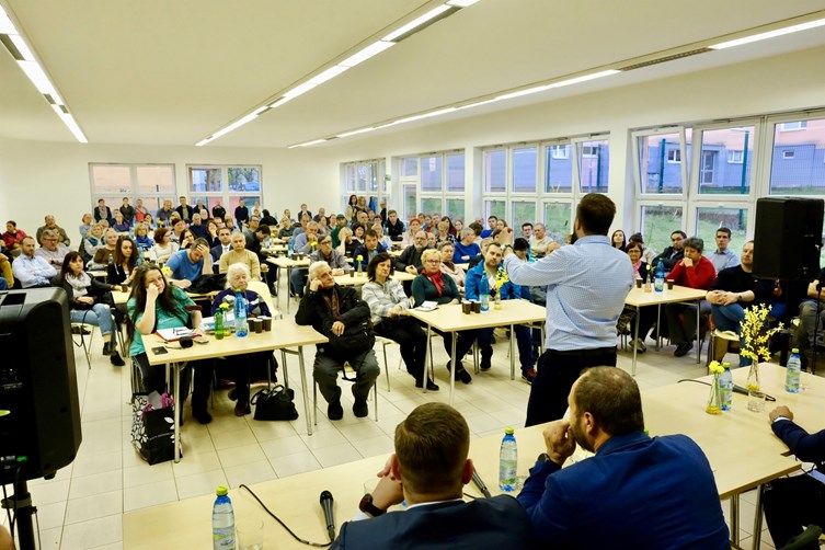 primátor bratislavy Matúš Vallo stojí pred obecenstom za ľavicami, pohľad je od chrbta vidieť Vallov chrbát a tváre hľadiska, miestnosť je plná ľudí